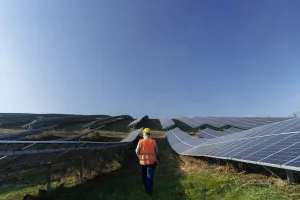 A technician walking between rows of solar panels at a photovoltaic plant, a typical scene for inspections and diagnoses carried out during solar energy consulting services in large-scale projects.