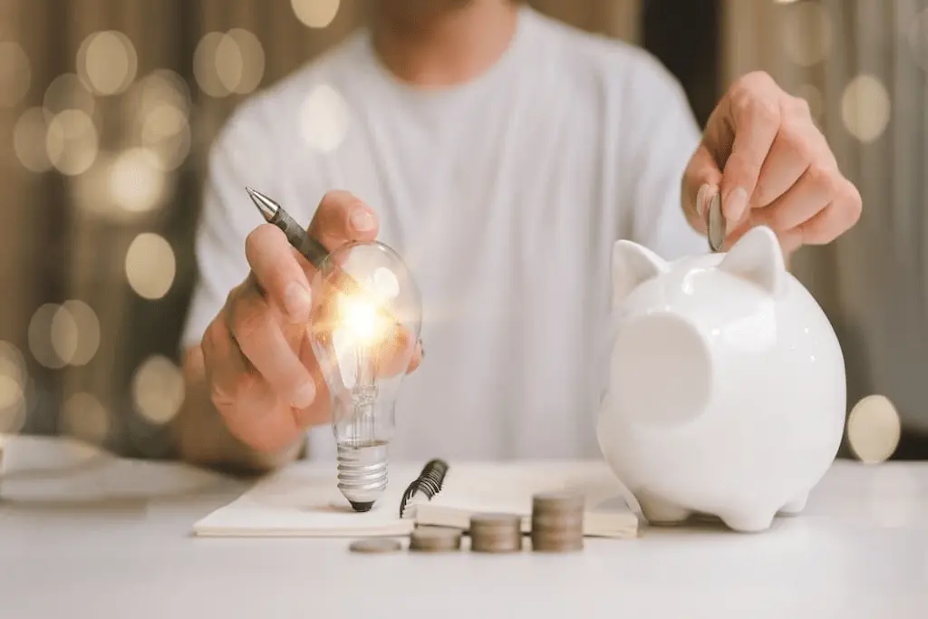 Economia de energia representada por lâmpada acesa e cofrinho para guardar dinheiro