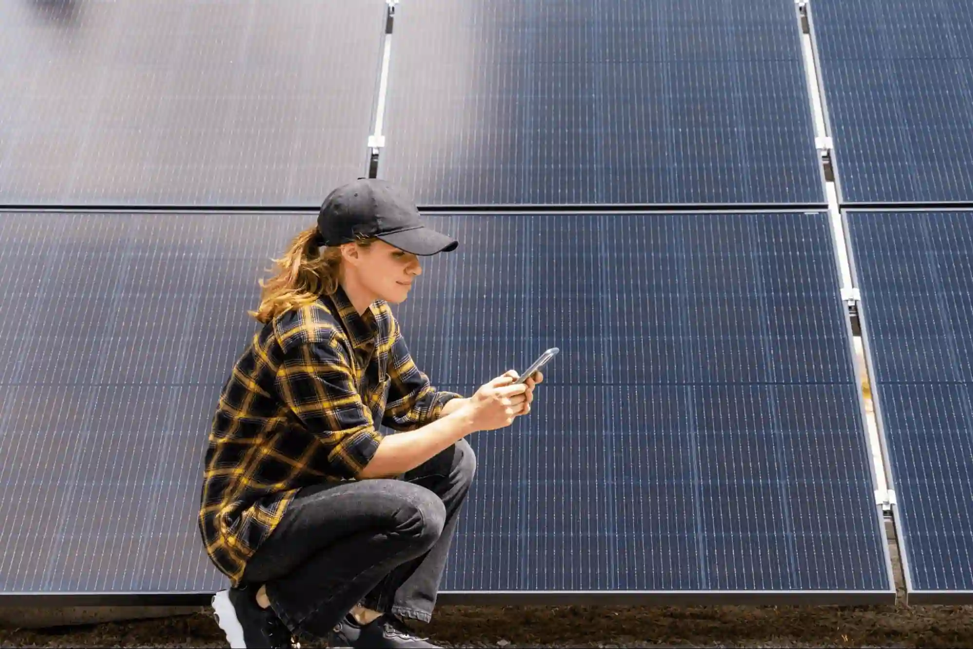 Profissional de energia solar usando smartphone para monitorar geração de eletricidade ao lado de painéis fotovoltaicos.